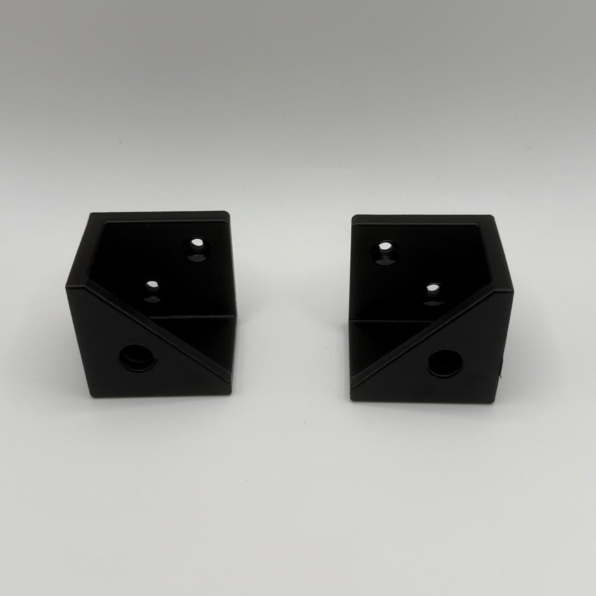 Two black metal mounting brackets with pre-drilled screw holes, shown side-by-side on a light gray background.
