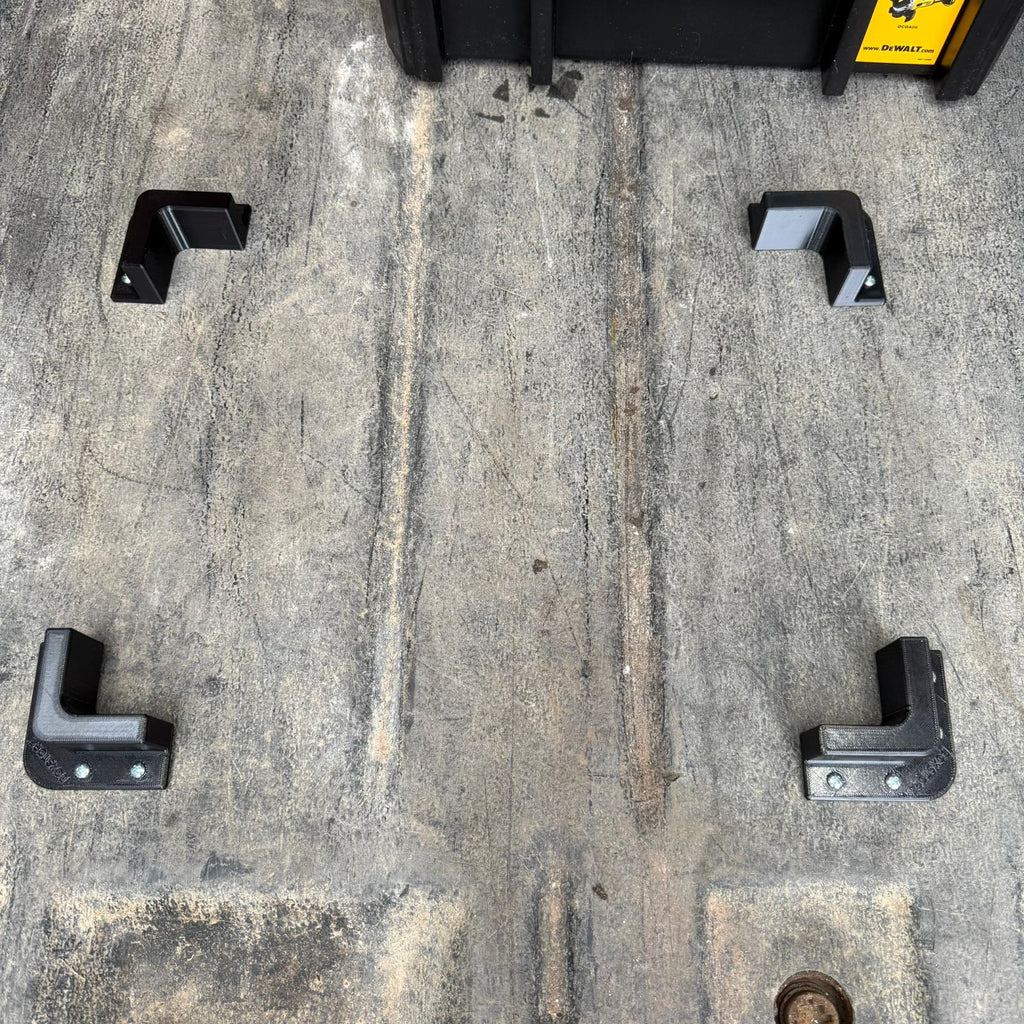 Set of four BoxStopz brackets screwed to a van floor around a toolbox