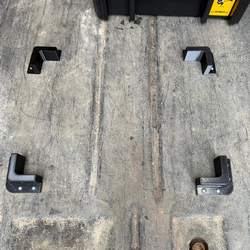 Set of four BoxStopz brackets screwed to a van floor around a toolbox
