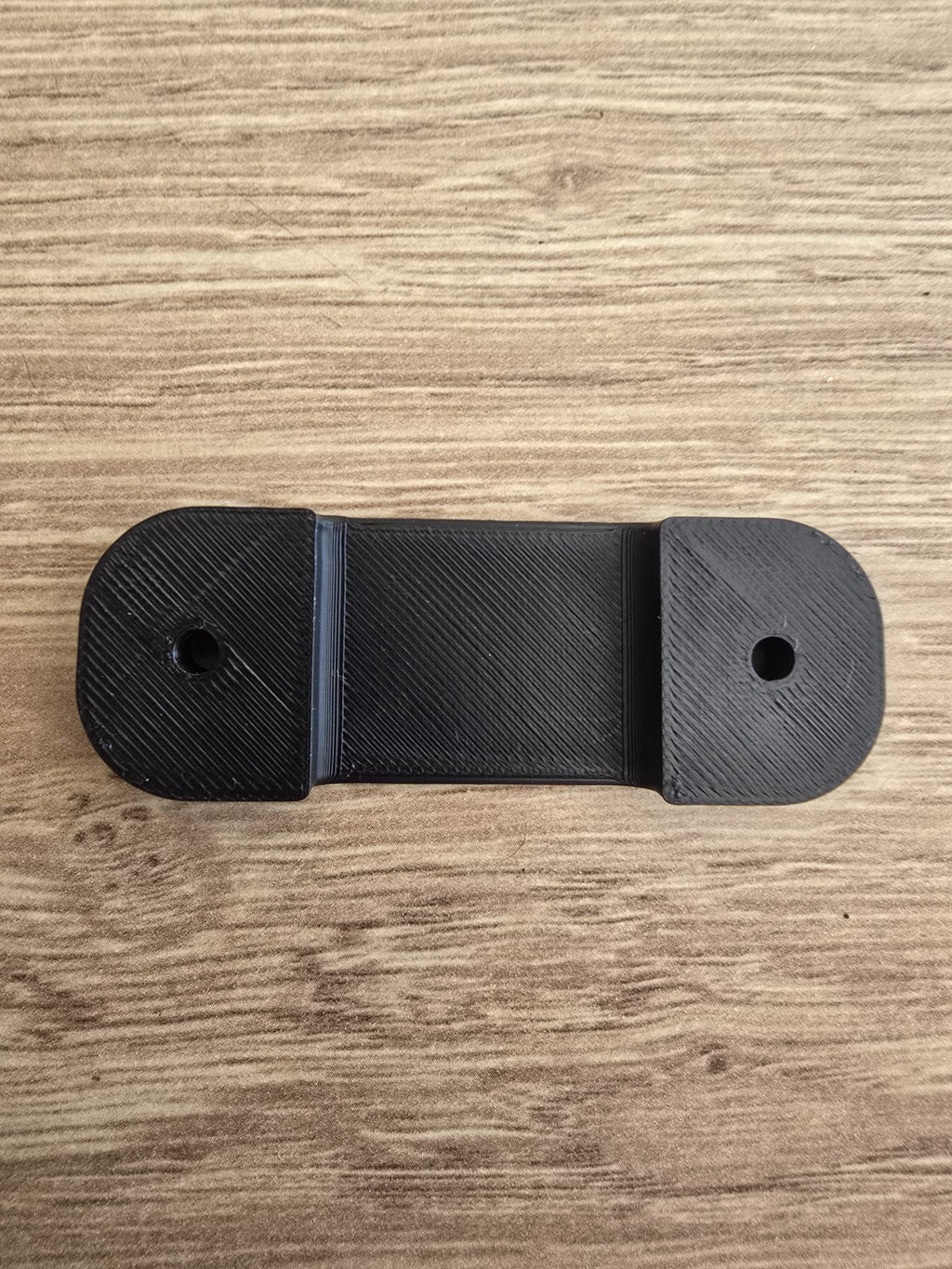 The tape measure holder laid flat, showing its slim oval shape and two countersunk screw holes.