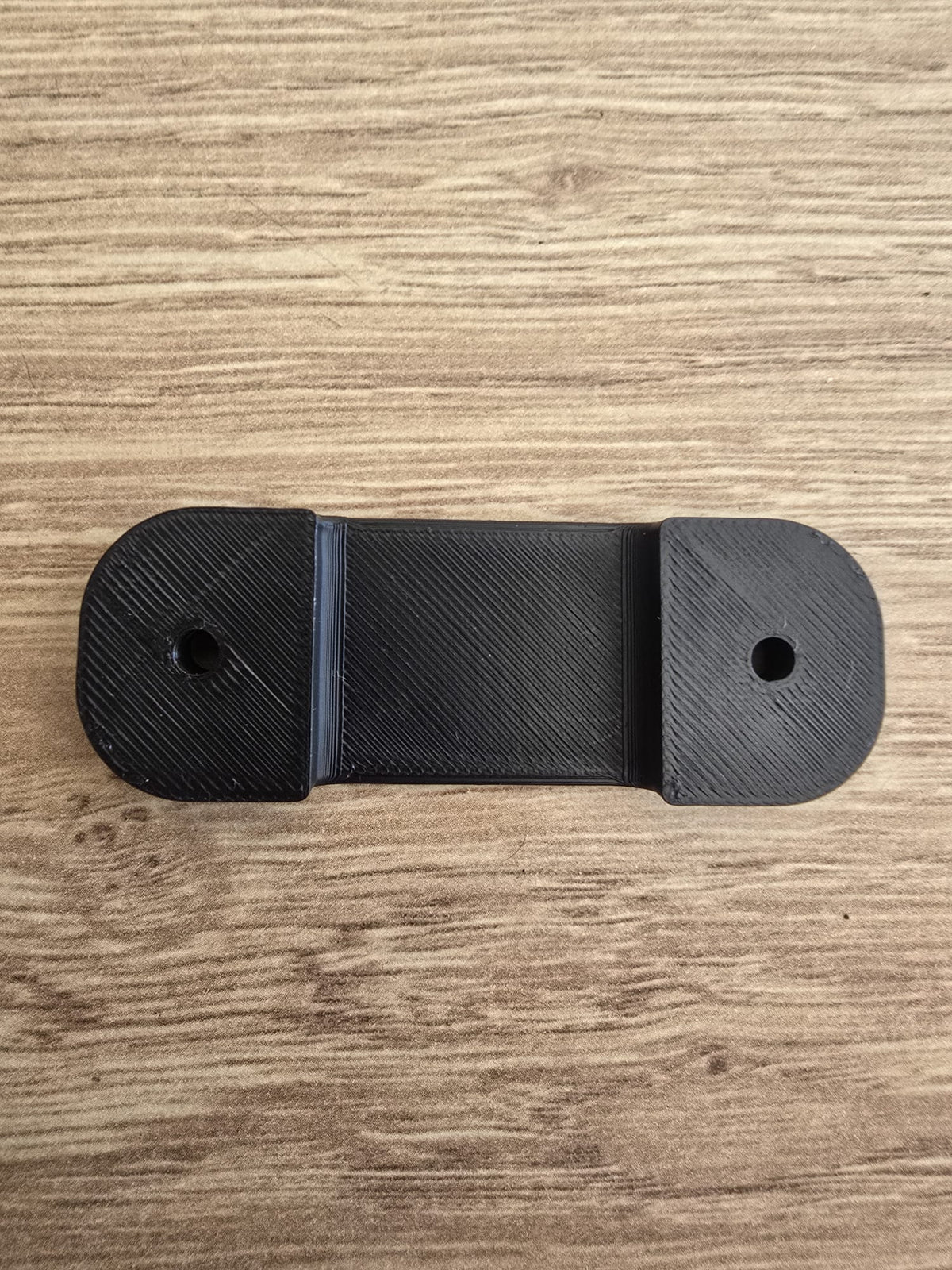 The tape measure holder laid flat, showing its slim oval shape and two countersunk screw holes.