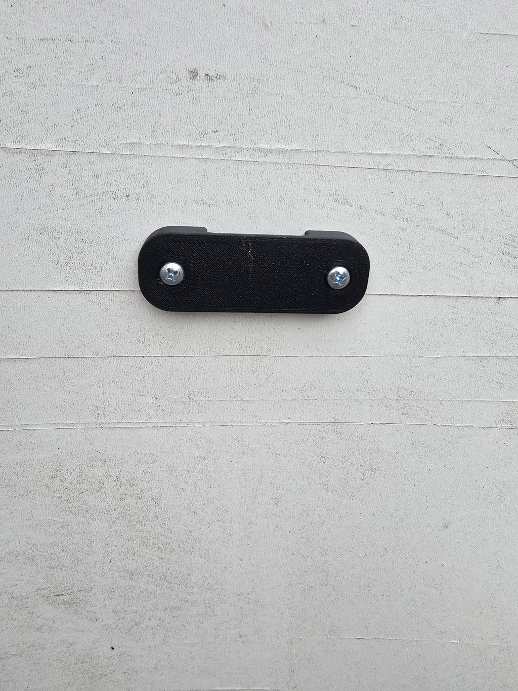The black tape measure holder screwed to a painted timber wall with two screws.